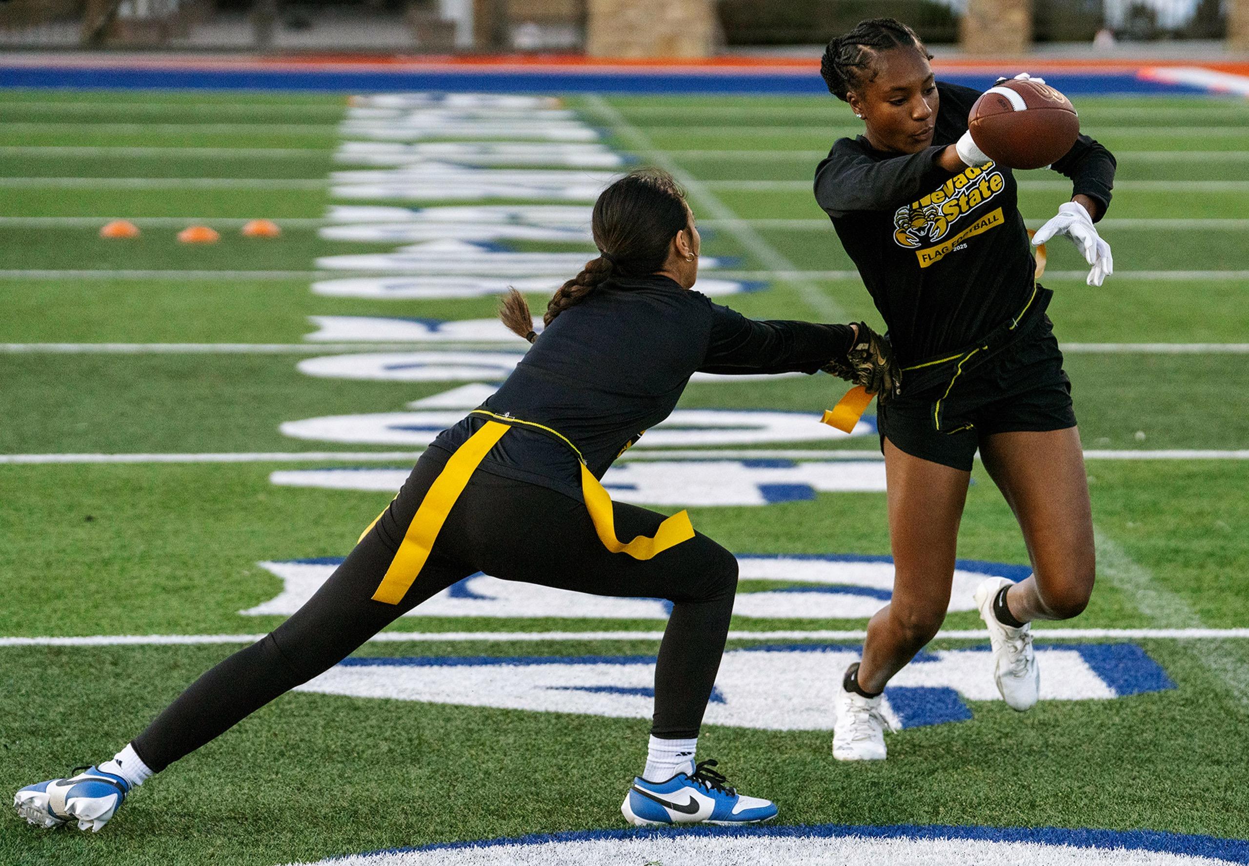 Two women's flag football team members practicing defensive formations in Nevada State practice uniforms
